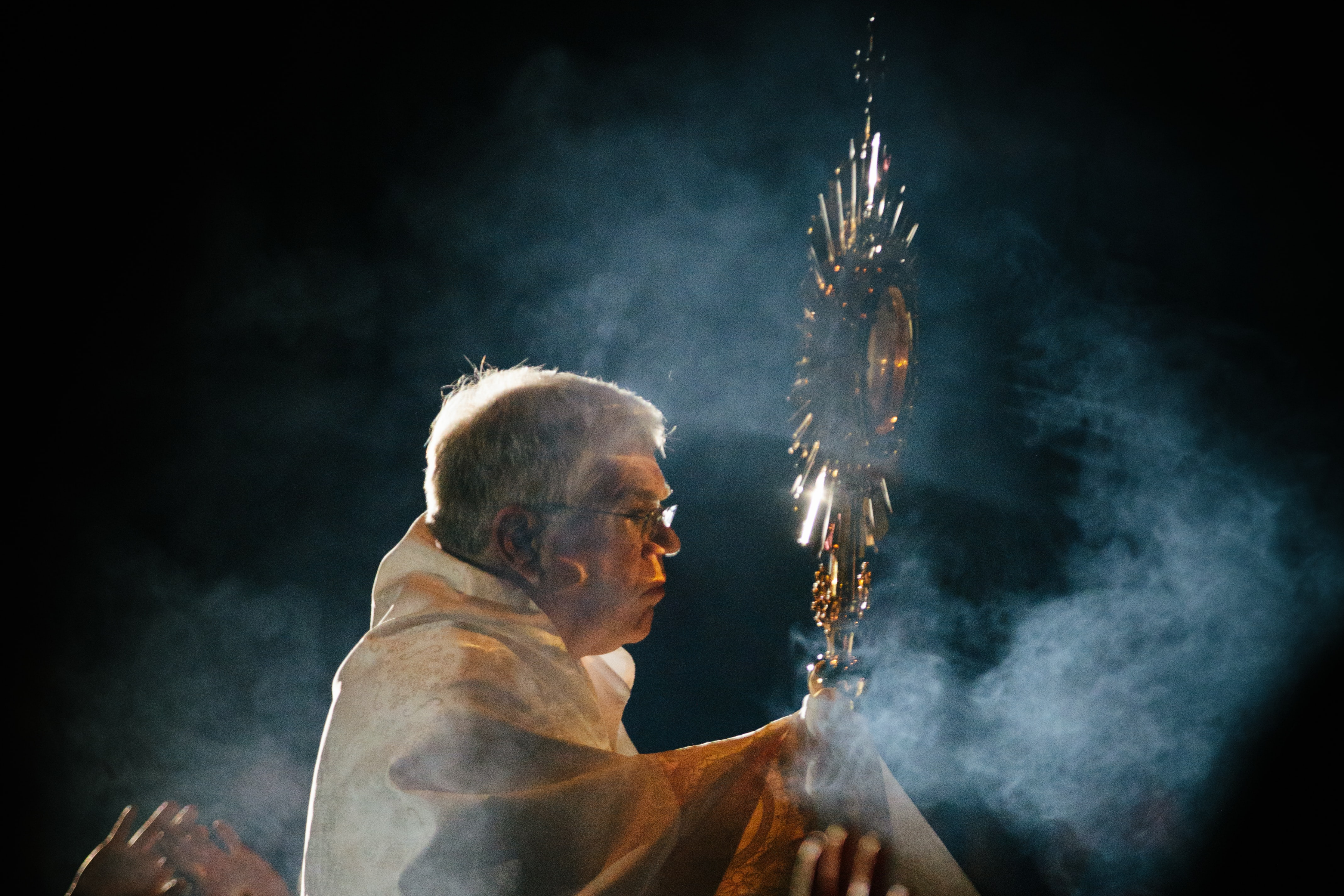 Photo of a priest holding up a monstrance containing Jesus in the Eucharist.